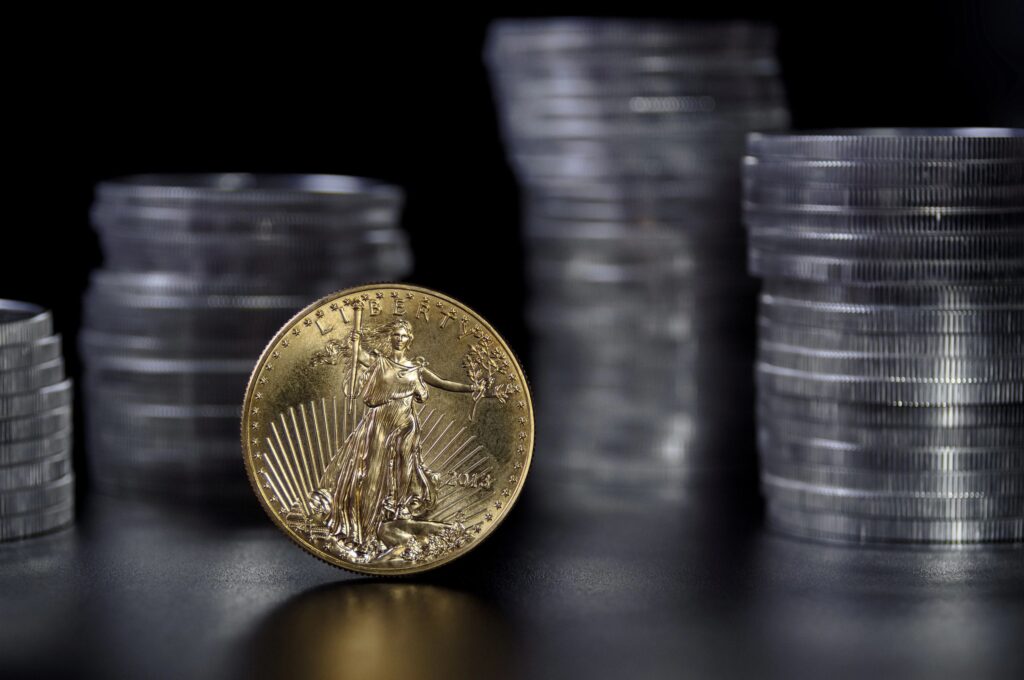 1 ounce gold coin infront of stacks of silver coins